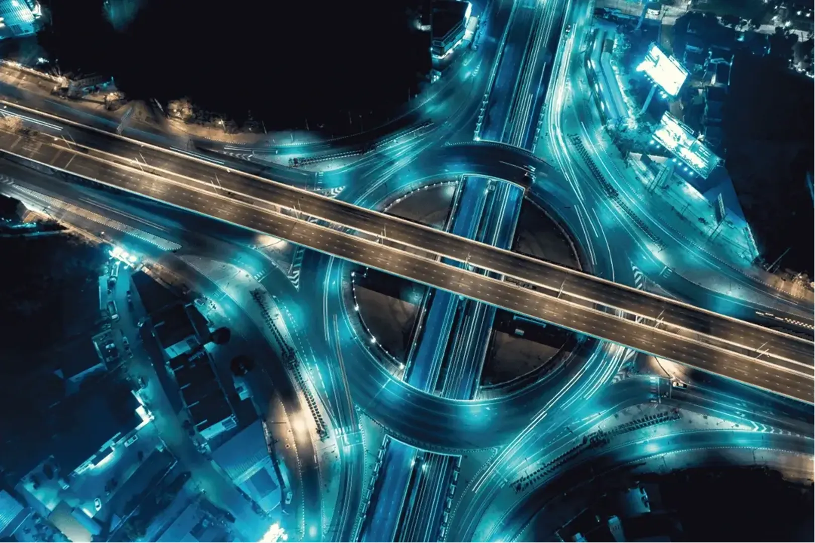 Aerial view of a highway intersection at night, showcasing the intricate network of roads and the vibrant city lights below.