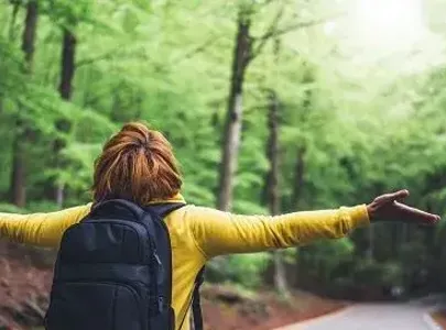 Person standing in a forest, arms spread looking up at the sky.